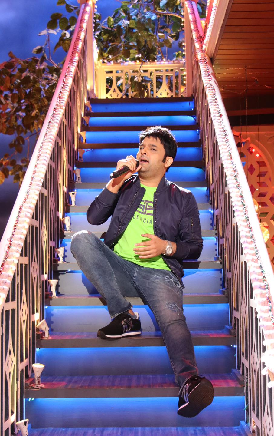 Kapil Sharma, sitting on a staircase, singing into a microphone