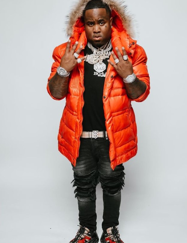 Mo3 in an orange puffer jacket against a light background