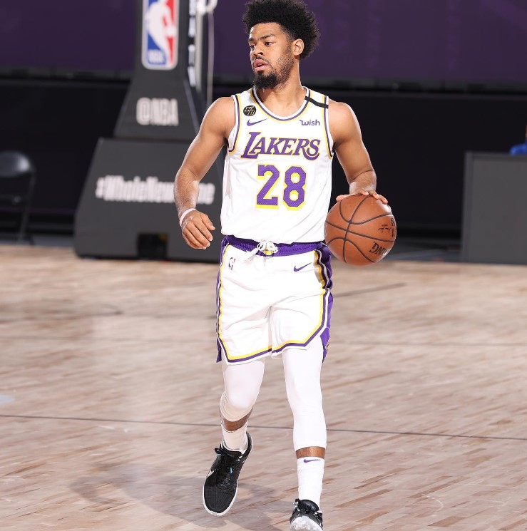 Quinn Cook wearing a white Lakers jersey at an indoor basketball court